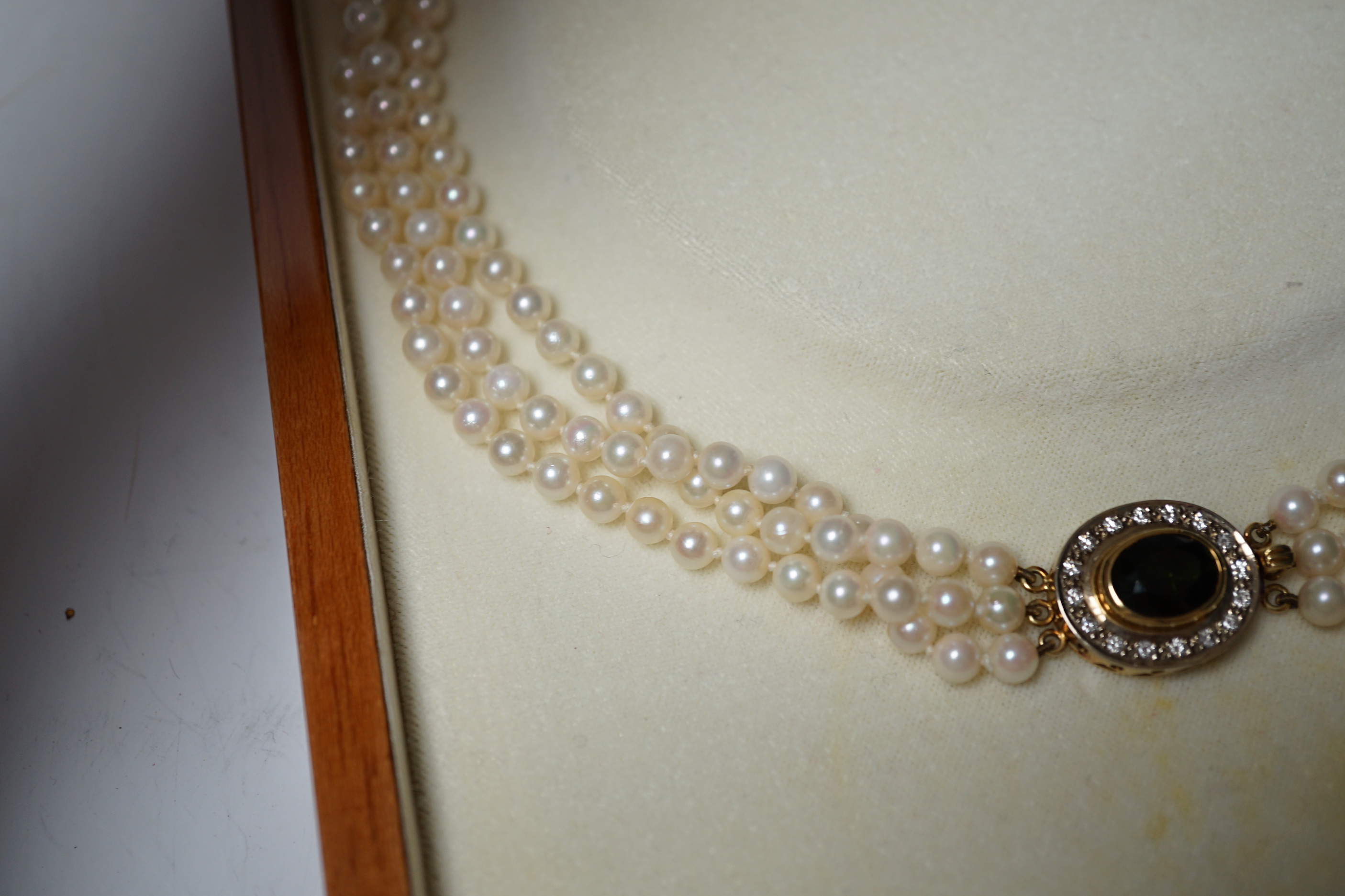 A modern triple strand cultured pearl necklace, with green tourmaline and diamond cluster set oval yellow metal clasp, 48cm.